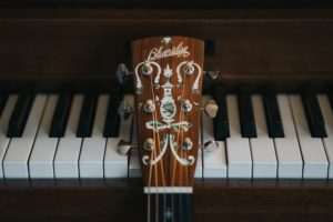 Dark brown wood guitar head in front of piano keys of a wood piano 